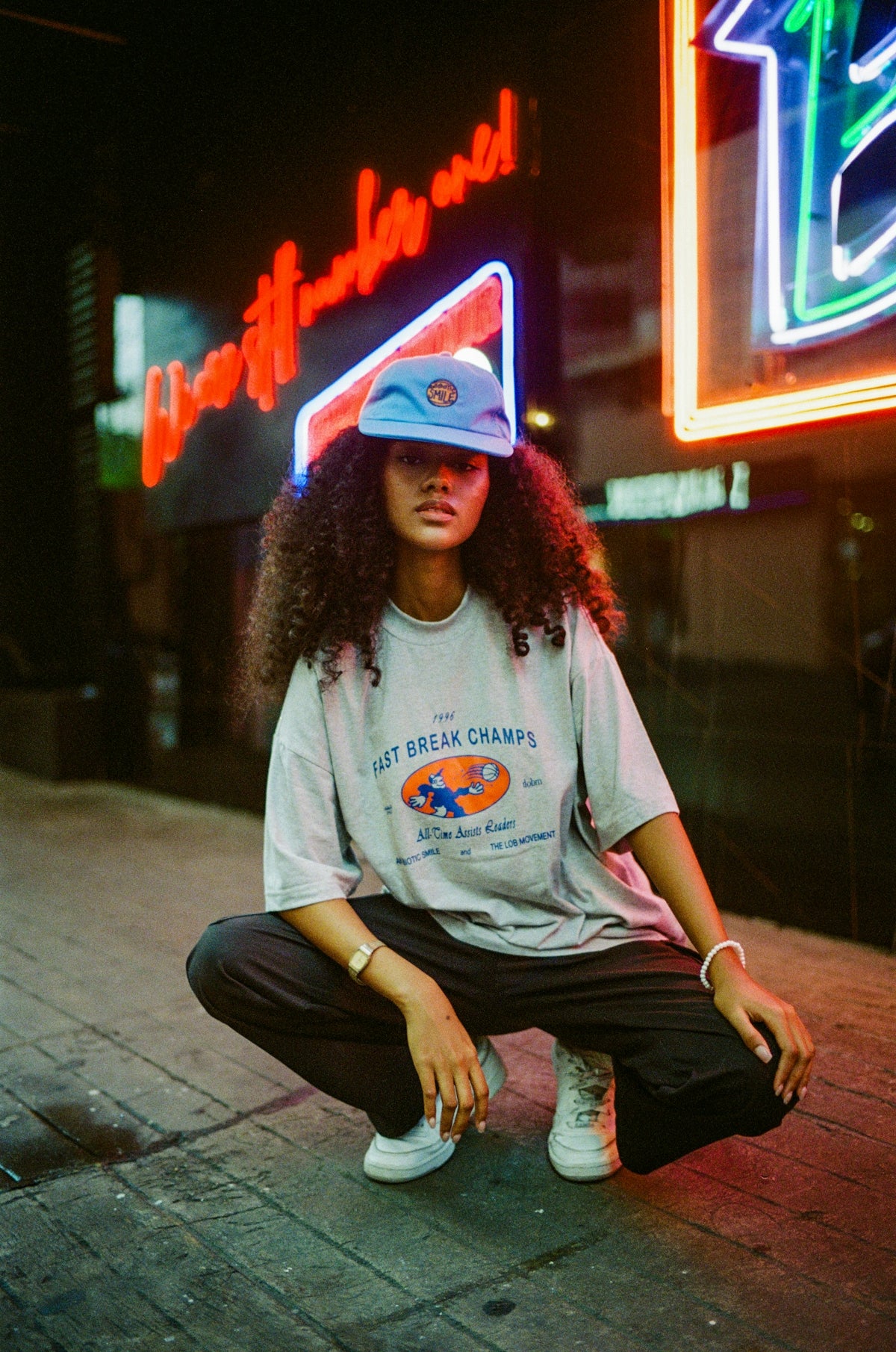 A woman sitting on the ground in front of a neon sign
