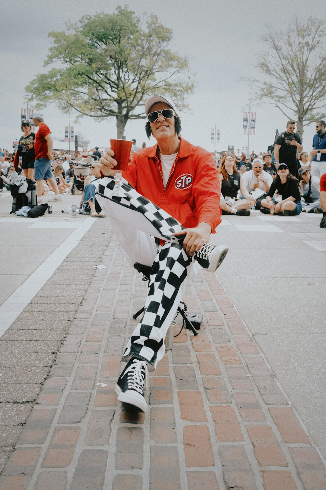 Man in red jacket and checkered pants on brick road.