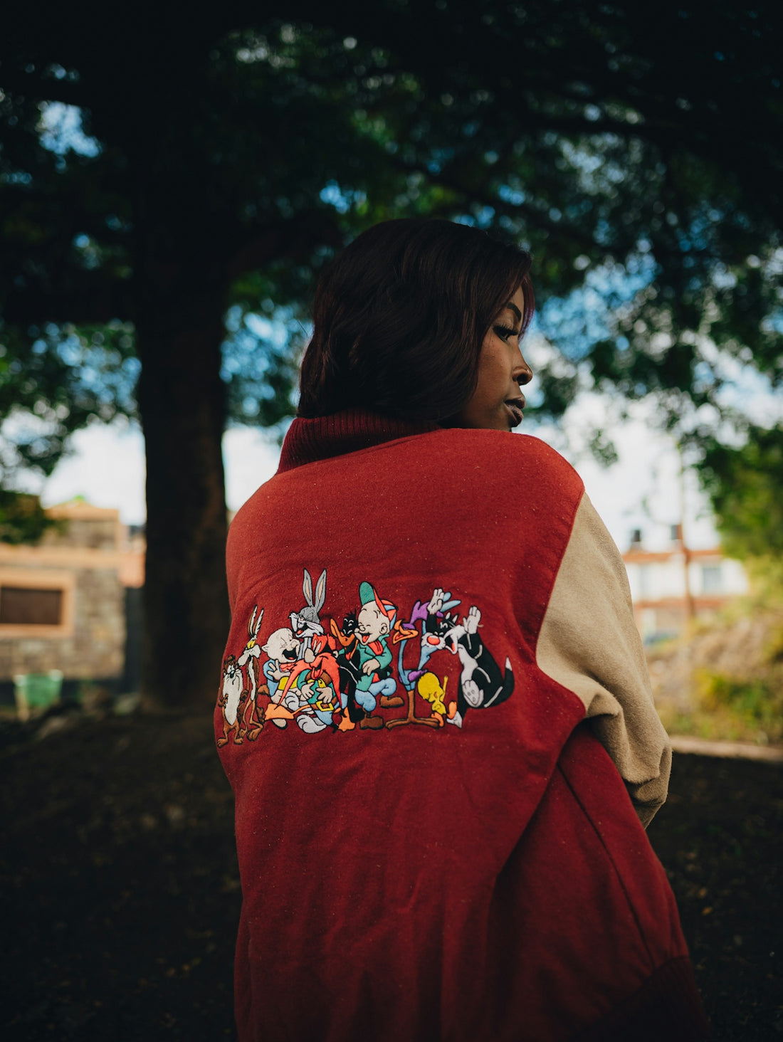 Woman wearing a red jacket featuring embroidered cartoon characters outdoors.