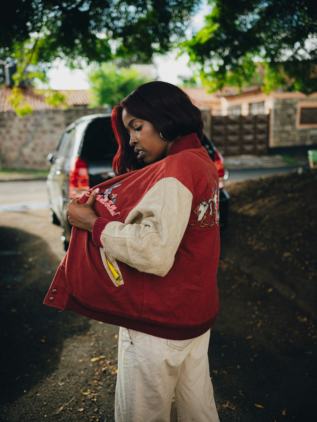 Young woman putting on a red and white jacket outside.