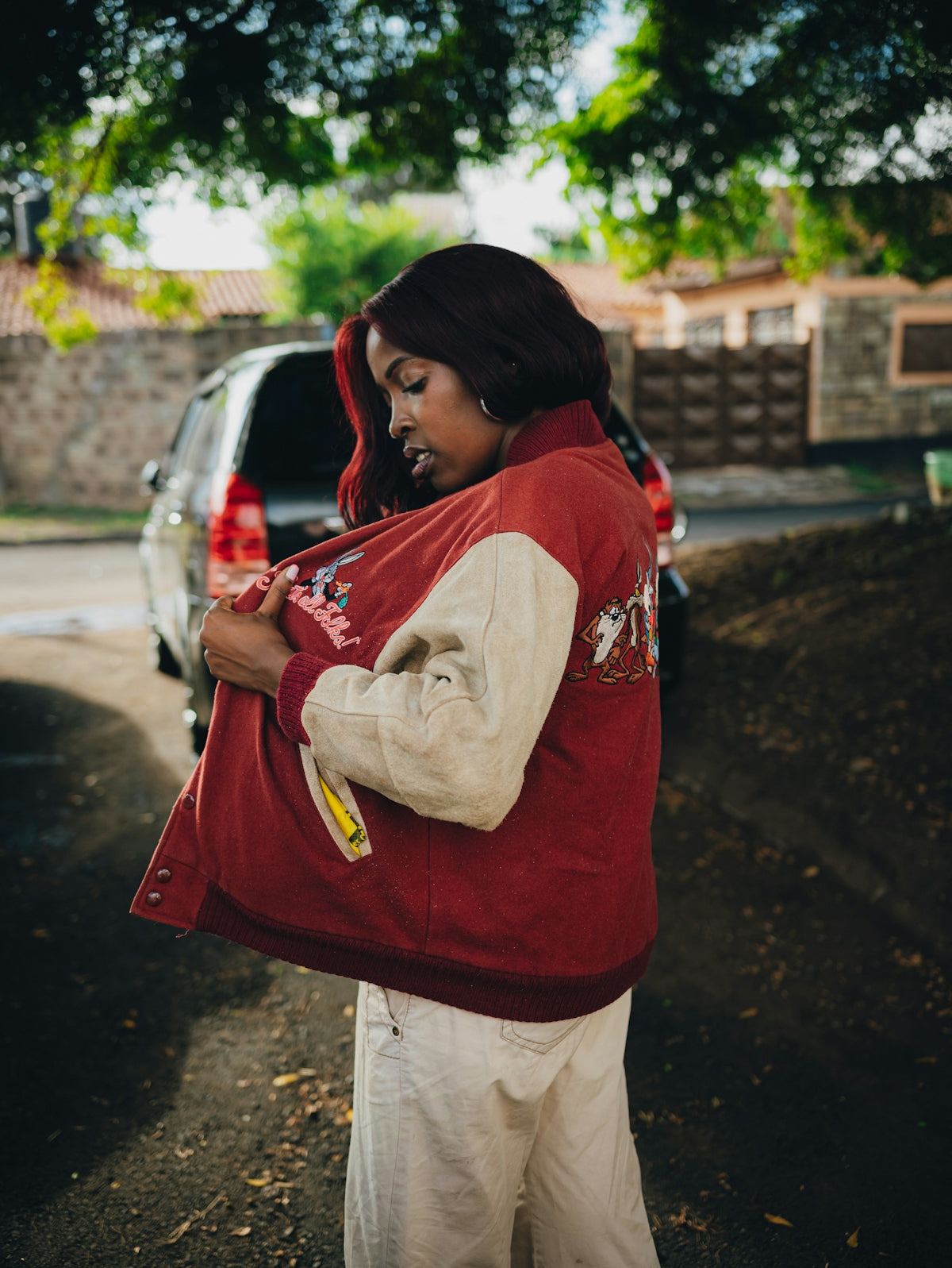 Young woman putting on a red and white jacket outside.
