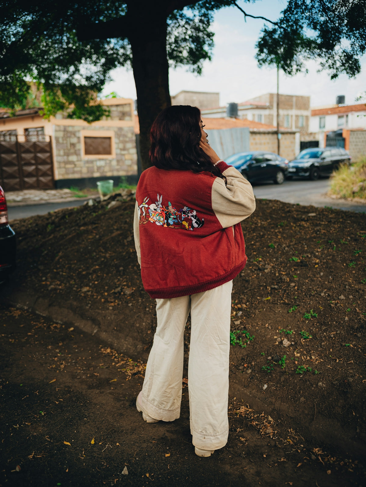 Woman in red jacket with cartoon characters stands outdoors.