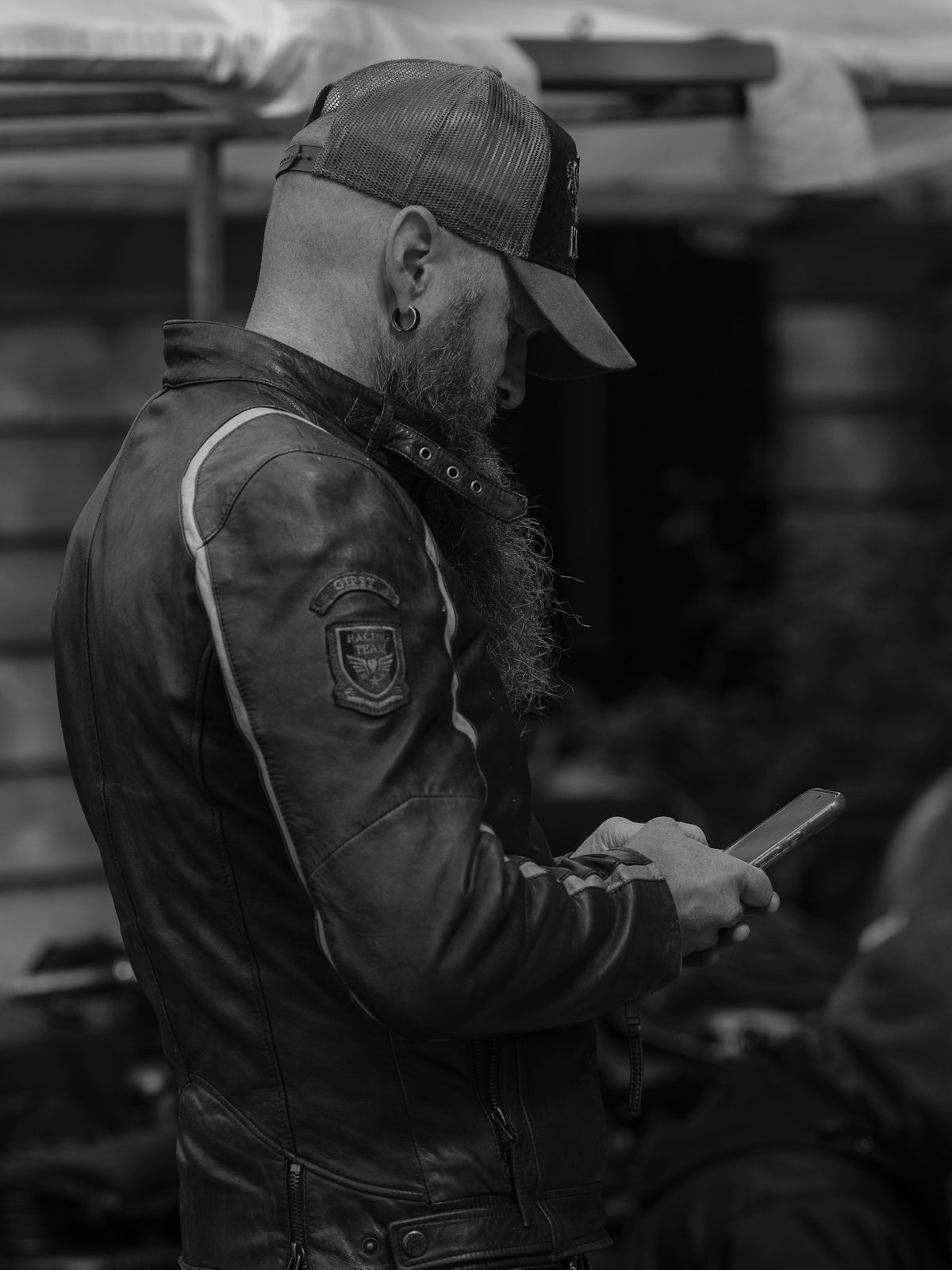 A bearded man in a leather jacket using a smartphone.